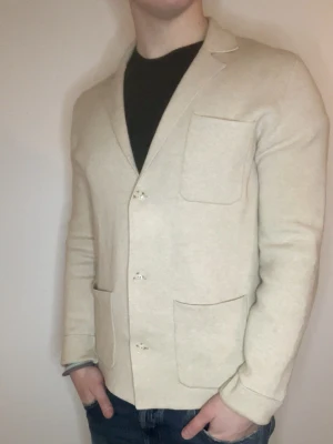 Beige stickad cardigan - Otroligt snygg beige stickad cardigan från bläck. Modellen är 180cm, 75kg.