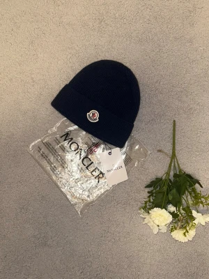 Mörkblå moncler mössan ull - Ribbstickad mörkblå mössa från Moncler med klassisk Moncler-logga framtill. Mössan har uppvikt kant och är tillverkad i mjuk ull, perfekt för kyliga dagar. Enkel och stilren design som passar till det mesta.Aktiv 24/7✅ Skickas inom 24h📦🚚 Kan gå ner i hugget 😃✅ Hör av er via frågor⁉️
