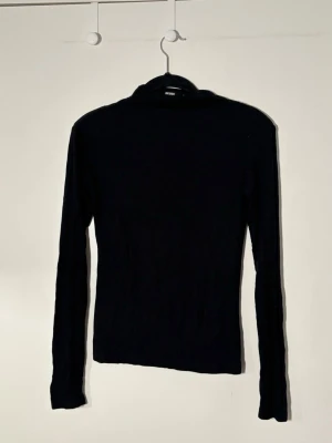 Svart polotröja från Bik Bok - En klassisk svart polotröja från Bik Bok med lång ärm och tight passform. Perfekt basplagg i garderoben, enkel att styla till <3 Tillverkad i mjukt material som känns skönt mot huden.