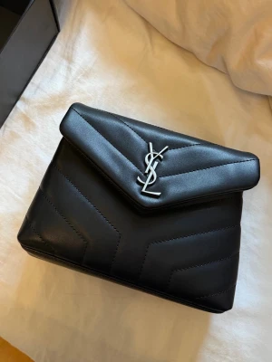 Svart ysl Loulou  - Ysl väska svart, ingår ett långt axelband! Endast använd ett fåtal gånger. Mått: L, 19 cm & H, 14 cm & B, 6 cm. En liten tråd som släppt inuti väskan (inget märkvärdigt) Och ett litet intryck på ena sidan (se sista bild) Säljs för att jag inte får användning för den. 😕  Har box, dustbag och kort. Inget kvitto 🩷 Pris går att diskutera 