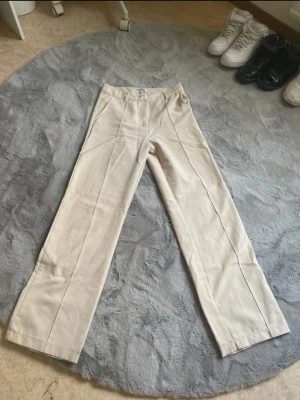 Beiga raka byxor från Madlady - Snygga beiga byxor från Madlady i rak modell. Byxorna har hög midja och är tillverkade i ett mjukt material. 