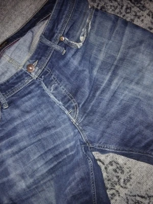 Jack&jones - Säljer ett par klassiska blå jeans från jack&jones med raka ben och normal passform. Jeansen har slitningar vid fickorna, femficksmodell och tydliga kontrastsömmar. Materialet är robust denim i bomull och färgen är mellanblå med tvättade detaljer.