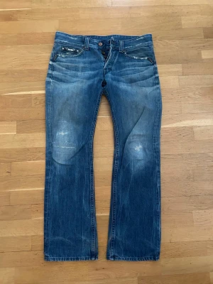 Blå bootcut jeans från WR (replay) - Säljer ett par blå bootcut jeans från WR (replay) med slitningar och snygga detaljer på fickorna. Jeansen har klassisk femficksdesign, normal passform och är tillverkade i tåligt denimtyg. Perfekta för dig som gillar en avslappnad och tidlös look.