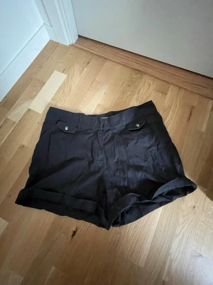Svarta shorts  - Svarta shorts från HPO Collection med uppvikta benslut och två fickor framtill med lock och knapp
