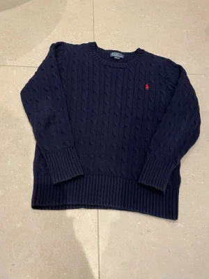 Mörkblå kabelstickad tröja Polo Ralph Lauren - Kabelstickad mörkblå tröja från Polo Ralph Lauren med klassisk röd logga broderad på bröstet. Har använts en gång. Priset kan gå ner lite vid snabbt köp.
