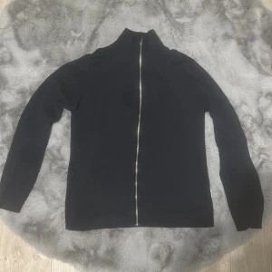 Mörkblå zip tröja - Säljer en mörblå zip från Lindbergh med hel dragkedja framtill. Tröjan har hög krage och långa ärmar, perfekt för lager-på-lager under kyliga dagar. Enkel och stilren design som passar till det mesta. Använd 3 gånger max.