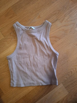 Beige ribbad linnetopp XS - Säljer en beige ribbad linnetopp i storlek XS. Toppen har en enkel och stilren design med breda axelband och rundad halsringning. Perfekt att matcha med jeans eller kjol för en avslappnad look.