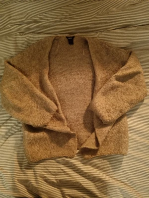 Beige stickad kofta från Lindex - Mysig beige stickad kofta från Lindex i storlek M/L, men passar mer som M. Koftan är öppen framtill, har lång ärm och är tillverkad i ett grovstickat material som känns både chill och varm. Perfekt att slänga på sig när det är lite kyligare ute. Lite nopprig. 