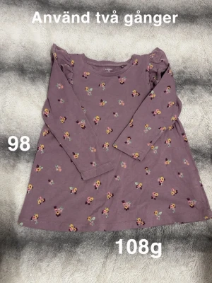 Lila blommig klänning från Lindex - Supersöt lila klänning från Lindex med små blommor i gult, rosa och grönt. Klänningen har långa ärmar och volangdetaljer vid axlarna. Perfekt för vår och sommar 🌸Använd två gånger. Storlek 98 