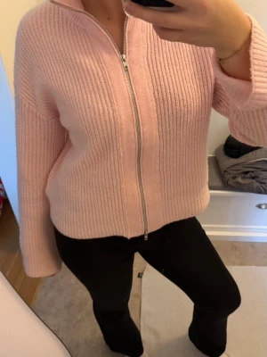 Ljusrosa stickad kofta med dragkedja - Mysig ljusrosa stickad kofta med hel dragkedja framtill. Tröjan har en ribbad struktur och lång ärm, perfekt för lager på lager under kyliga dagar💕