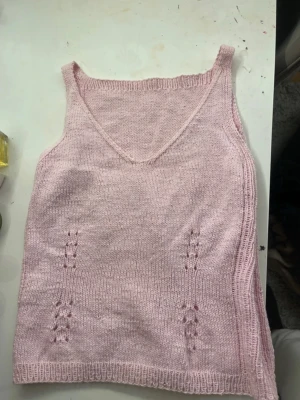 Ljusrosa stickad linnetopp - Supersöt ljusrosa stickad linnetopp med v-ringning och smala axelband. Toppen har fina hålstickade detaljer framtill som ger en extra touch. Perfekt till sommaren och enkel att styla med jeans eller kjol.