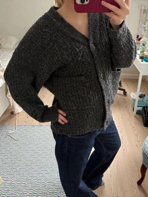 Mörkgrå stickad kofta från lager 157 - Mysig mörkgrå stickad kofta från lager 157 i oversized modell. Koftan har stora knappar framtill, två fickor och långa ärmar. Perfekt för lager-på-lager och chill dagar. Snyggt grovstickat material som ger en cool och avslappnad vibe.