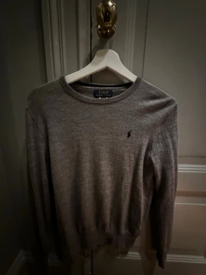 Grå tröja från Polo Ralph Lauren - Säljer en stilren grå tröja från Polo Ralph Lauren i storlek XL. Tröjan har rund halsringning, lång ärm och den klassiska lilla broderade loggan på bröstet. Perfekt till både jeans och chinos för en clean look.