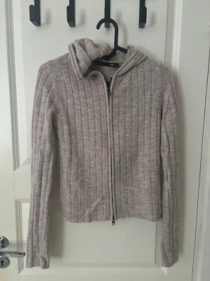 Beige ribbad hoodie med dragkedja - Mysig beige hoodie från Lager157 med ribbad struktur och dragkedja framtill. Tröjan har huva och långa ärmar, perfekt för kyliga dagar. Materialet känns mjukt och är stickat för extra komfort. Enkel att matcha med jeans eller leggings.