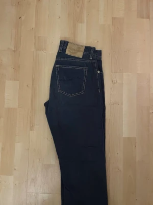 Jacob Cohen 610 Special blå jeans - Snygga blå jeans från Jacob Cohen, modell 610 Special. De har kontrastsömmar, klassisk femficksdesign och knappgylf med märkets logga. Materialet är jeans med exklusiv känsla och detaljer som broderad J på fickan. Perfekt för dig som gillar stilrena och lyxiga jeans.