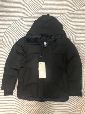 Svart dunjacka från Canada Goose M - Säljer en svart dunjacka från Canada Goose i storlek M. Jackan har huva, dragkedja och klassisk Canada Goose-logga på ärmen. Perfekt för kalla dagar och riktigt snygg streetstil. Jackan är vadderad och har en clean look utan onödiga detaljer.