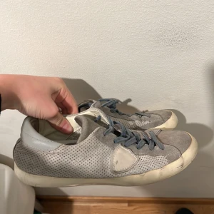 Philip model - Snygga grå sneakers med perforerat mönster på sidorna och matchande grå snörning. Skorna har rund tå och platt sula, vilket ger en klassisk och avslappnad look. Perfekta för dig som gillar stilrena och enkla sneakers.