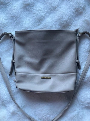 Ljusgrå axelväska från Björn Borg - Stilren ljusgrå axelväska från Penthouse i mjukt syntetmaterial. Väskan har en enkel, slät design med justerbar axelrem och en liten guldfärgad logga framtill. Perfekt för dig som gillar minimalistisk stil.