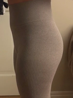 Ribbade leggings - Säljer ett par ribbade leggings i en mjuk brun nyans. De har hög midja och är tillverkade i stretchigt material som sitter tight och bekvämt. Perfekta för chill eller träning, och den ribbade strukturen ger en snygg touch.