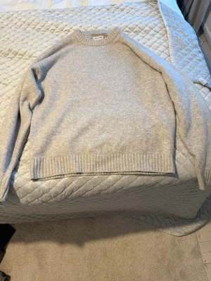 Ljusgrå stickad tröja från Jack&jones  - Mysig ljusgrå stickad tröja från jack&jones i klassisk modell. Tröjan har rund halsringning, ribbstickade muddar och nederkant. Perfekt för lager på lager och enkel att matcha med olika stilar.