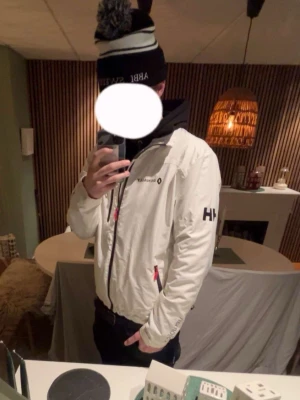 Vit Helly Hansen Renault vindjacka - Snygg vit vindjacka från Helly Hansen med Renault-logga och texten 'Passion for life' på ryggen. Jackan har dragkedja framtill, svarta detaljer och HH-logga på ärmen. Perfekt för dig som gillar sportig stil och vill sticka ut.