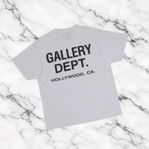 Ljus Grå t-shirt från Gallery Dept. - Ljus grå t-shirt från Gallery Dept. med tryck fram och stort tryck på ryggen.