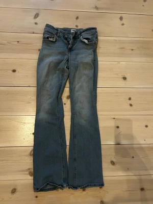 Blå bootcut jeans  - Ett par klassiska blå jeans med bootcut passform och slitna detaljer vid bensluten. Jeansen har fem fickor, normal midja och är tillverkade i tåligt denimtyg av bomull. Perfekta för en avslappnad och trendig look. Ngt många för mig som är 164 cm.