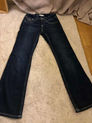 Mörkblå bootcut jeans med kontrastsömmar - Snygga mörkblå jeans med bootcut passform och tydliga vita kontrastsömmar. Klassisk femficksmodell med knapp och dragkedja framtill. Perfekta för dig som gillar en lite vidare siluett nertill.