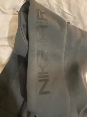 Gråa Nike Air mjukisbyxor - Mörkgrå mjukisbyxor från Nike Air med tryckt logga längs benet. Sköna och stilrena byxor i mjukt material, perfekta för chill eller träning. Klassisk passform med resår i midjan och benslut. Plus om du tvättar den för mycket så sliter ut fibrerna snabbare, bleker färger.