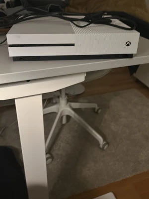 Vit Xbox One S spelkonsol - Säljer en vit Xbox One S spelkonsol med stilren design och matta ytor. Konsolen har en rektangulär form och är tillverkad i plast. Perfekt för gaming och streaming, HDMI-kabel medföljer inte. Bara strömkabel 
