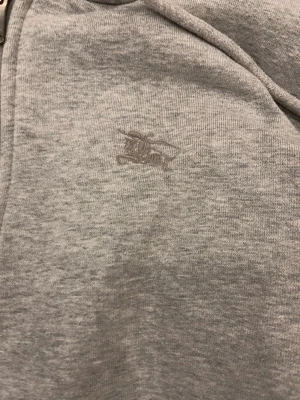 Grå zip hoodie från Burberry - Säljer en grå hoodie från Burberry med dragkedja och klassiskt rutigt foder i huvan. Hoodien har fickor framtill och en diskret broderad logga på bröstet. Perfekt för dig som gillar stilrena och exklusiva plagg med en twist. Skulle uppskatta att tröjan passar de som är 170-175 då tröjan är lite för liten för mig på längden och är 180cm. Tröjan är en rep. Använd ca 3 gånger