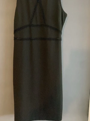 Svart ärmlös kort klänning - Stilren svart ärmlös klänning med dekorativa spetsdetaljer i midjan och över bysten. Klänningen har en rak, kroppsnära passform och slutar ovanför knäna. Perfekt för dig som gillar minimalistisk och elegant stil.