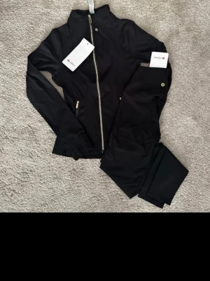 lululemon Set – jacka & Byxor – Svart – Strl XS – Perfekt träningsset 🖤 - Säljer ett stilrent och funktionellt lululemon-set bestående av jacka med dragkedja och matchande byxor. Ett mycket populärt set som passar perfekt för träning, yoga, promenader eller som snygg athleisure till vardags.  🔹 Märke: lululemon 🔹 Storlek: XS (både jacka & byxor) 🔹 Färg: Svart 🔹 Set: Jacka + byxor 🔹 Passform: Figurnära / sportig 🔹 Skick: Mycket bra skick – inga hål, fläckar eller synligt slitage 