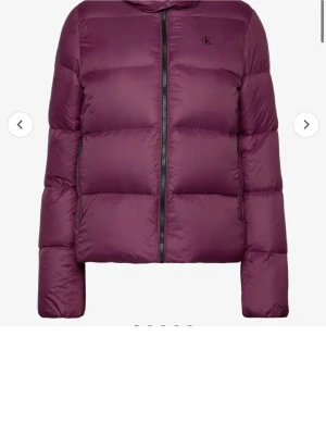 Mörklila pufferjacka från Calvin Klein - Snygg mörklila pufferjacka från Calvin Klein med diskret logga på bröstet. Jackan har quiltad design, dragkedja framtill och långärmad passform. Perfekt för kyliga dagar och ger en trendig look.