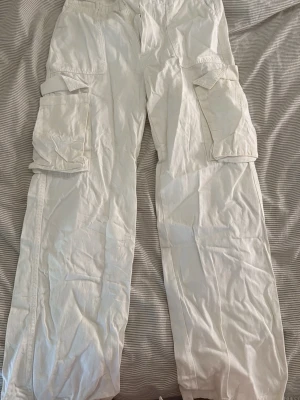 Vita cargopants med stora fickor - Säljer ett par vita cargopants med flera stora fickor på sidorna och baktill. Byxorna har en loose passform och är perfekta för en avslappnad streetwear-look. Tillverkade i bomull för skön känsla och enkel styling.