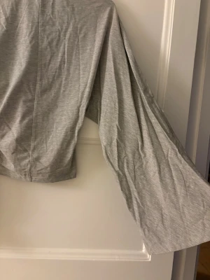 Grå långärmad croppad topp - Snygg grå croppad topp med långa utsvängda ärmar och enkel design. Tillverkad i mjukt bomullsmaterial som känns skönt mot huden. Perfekt att matcha med jeans eller kjol för en trendig look. 