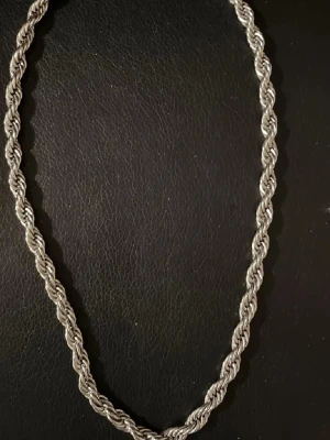 Silverfärgat tvinnat halsband - Säljer ett stilrent halsband i silverfärg med tvinnad kedja. Halsbandet har en klassisk design som passar perfekt till olika stilar. Inget synligt märke på halsbandet. Perfekt accessoar för dig som gillar minimalistiska smycken.