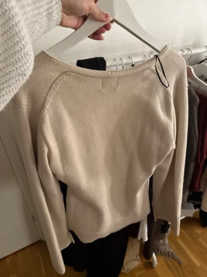 Beige stickad tröja med v-ringning - Säljer en stilren beige stickad tröja med v-ringad hals och långa ärmar. Tröjan har en enkel, rak passform och ribbstickade muddar vid ärmslut och nederkant. Perfekt basplagg i mjukt material som passar till det mesta.