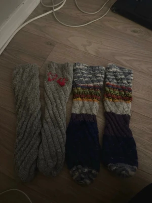 Stickade ullstrumpor i olika färger - Två par stickade ullstrumpor, ett par i grått med tvinnat mönster och ett par i blått, grått och flerfärgat randigt. Perfekta för kalla dagar och mysiga hemmakvällar. Handgjorda känsla och unika detaljer. Storlek vet jag ej då min gammelfarmor har stickad de men mellan 35-38 