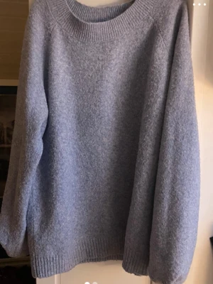 Ljusblå oversized stickad tröja - Mysig ljusblå stickad tröja med rund halsringning och ribbade muddar vid ärmslut och nederkant. Tröjan har en avslappnad, oversized passform och är perfekt för lager på lager. Materialet ser ut att vara mjukt och fluffigt, troligen en ull- eller akrylblandning.