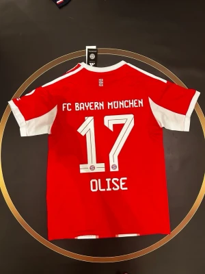 Bayern München matchtröja röd - Röd Bayern München matchtröja med vita detaljer och nummer 17 samt namnet Olise på ryggen. Tröjan har klubbens logga och är tillverkad i ett lätt och ventilerande material, perfekt för fotbollsträning eller match. S och L