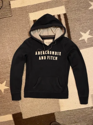 Abercrombie & Fitch hoodie - Mörkblå Abercrombie & Fitch hoodie med vit broderad A&F-logga på bröstet. Mjuk insida i ljusgrått tyg. Tröjan är i storlek M men sitter som en S. Tröjan är i mycket gott skick! Hör av dig vid minsta fundering.😁🙌