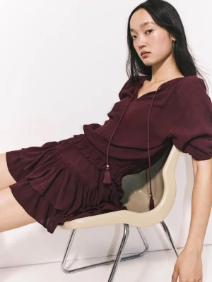 Vinröd volangklänning med snörning - Vinröd kortklänning med volanger och puffärmar. Klänningen har v-ringning med snörning och avslappnad passform i midjan. Tillverkad i ett lätt, vävt material som ger en luftig känsla. Perfekt för dig som gillar trendiga detaljer och en feminin look.