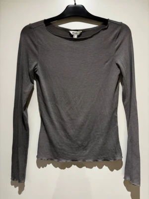 Grå långärmad topp från VERO MODA - En enkel och stilren grå långärmad topp från VERO MODA. Modellen är figurnära med rund halsringning och vågig kant nertill. 