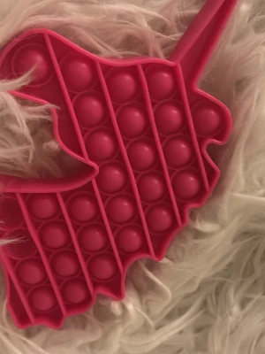 Röd enhörning pop it accessoar - Säljer en rosa pop it i form av en enhörning. Tillverkad i mjuk silikon och perfekt som stressleksak eller accessoar till väskan. Den har flera bubblor att trycka på och en unik enhörningsdesign.