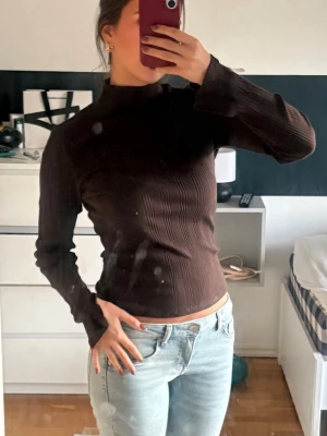 Brun ribbad långärmad tröja - Snygg brun långärmad tröja med ribbat mönster och hög hals. Långa ärmar med en slit längst ner. Så snygg och stilren. 