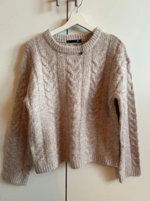 Beige kabelstickad tröja 157 - Mysig beige kabelstickad tröja. Helt ny stickad tröja från Lager 157 i storlek Small. Aldrig använd, men prislappen saknas. Jättefint grovstickat flätmönster och väldigt mjuk kvalitet. Axel 50 cm, längd 60 cm 