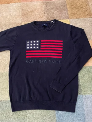 Mörkblå stickad tröja från Gant - Mörkblå stickad tröja från Gant med amerikanska flaggan på. Storlek M. Skriv vid funderingar.