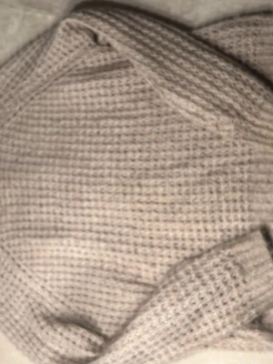 Beige stickad tröja med struktur - Beige stickad tröja med grovt, rutigt strukturmönster. Tröjan har långa ärmar och ribbstickade kanter. Perfekt för lager-på-lager och enkel att matcha med olika outfits.