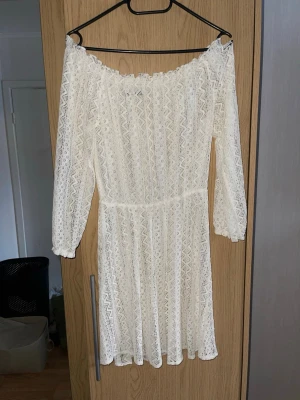 Vit spetsklänning från Rut&Circle - Superfin vit kortklänning från Rut&Circle i spets med offshoulder och trekvartsärm. Klänningen har ett vackert spetsmönster och är perfekt för sommarens alla tillfällen. Snygg passform och romantisk känsla.